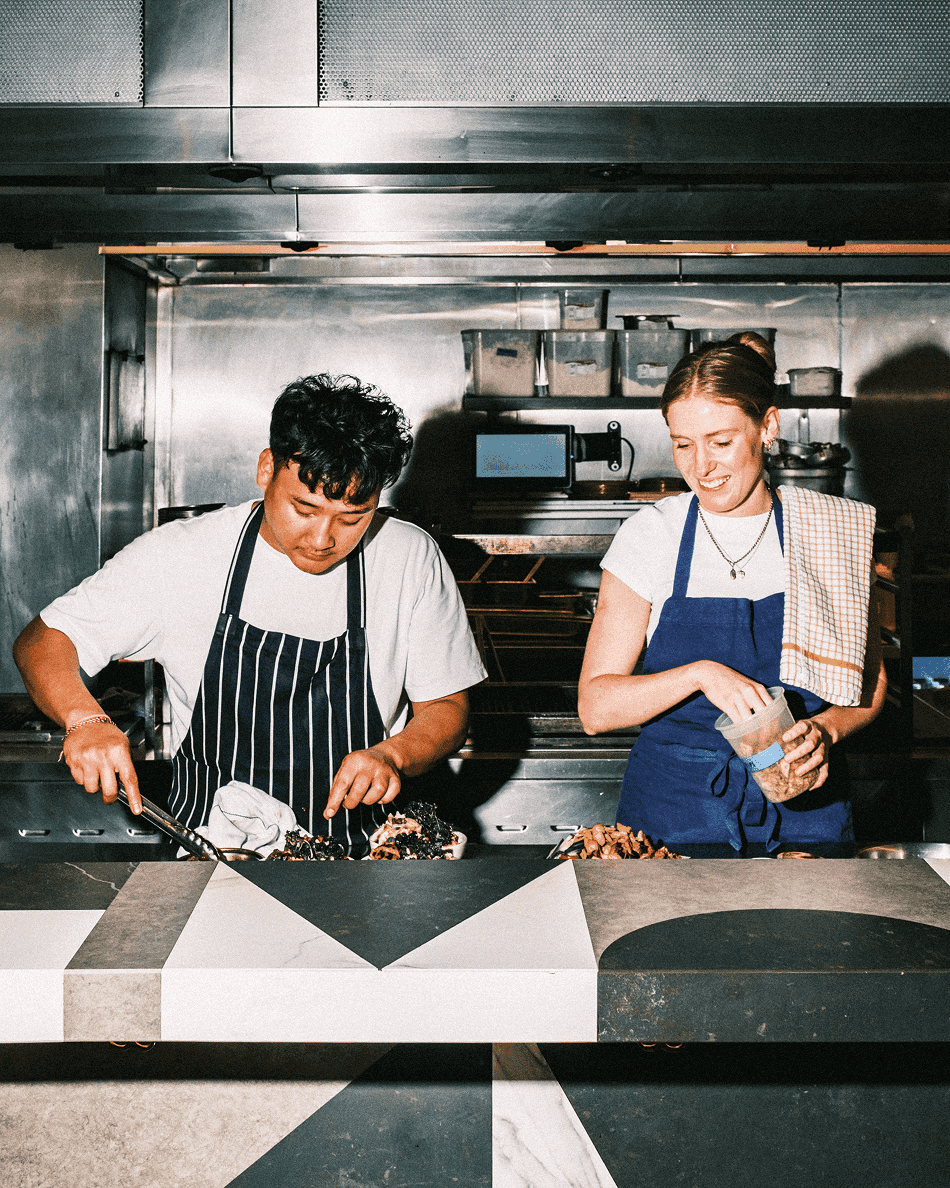 Two chefs in aprons cooking together in a professional kitchen